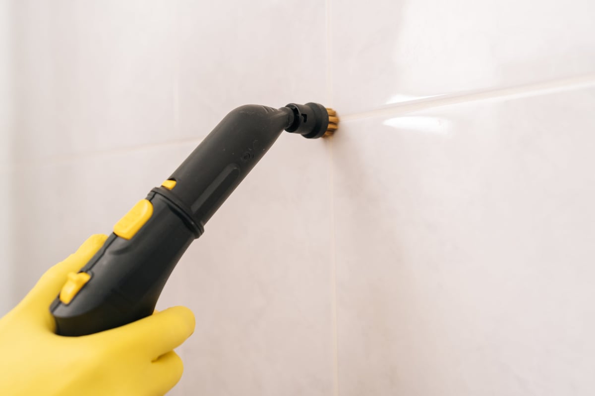 Close-up of a gloved hand steam cleaning tile grout in a bathroom