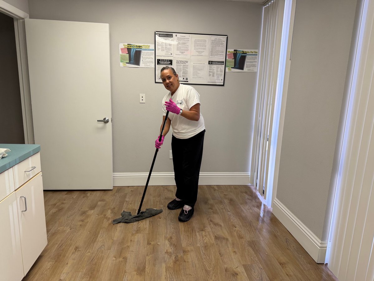 Team member in pink gloves sweeping a wooden floor with a black broom in an office